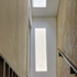 Loft Stairwell: A large roof-light brings light into the narrow stairwell, reflecting diffuse light from the sealed rough plaster wall and mild steel stair